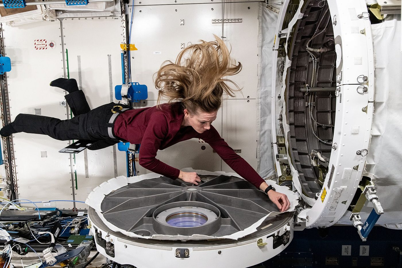 A NASA astronaut floats beside an open circular hatch while opening the airlock of the Kibo laboratory module aboard the International Space Station.