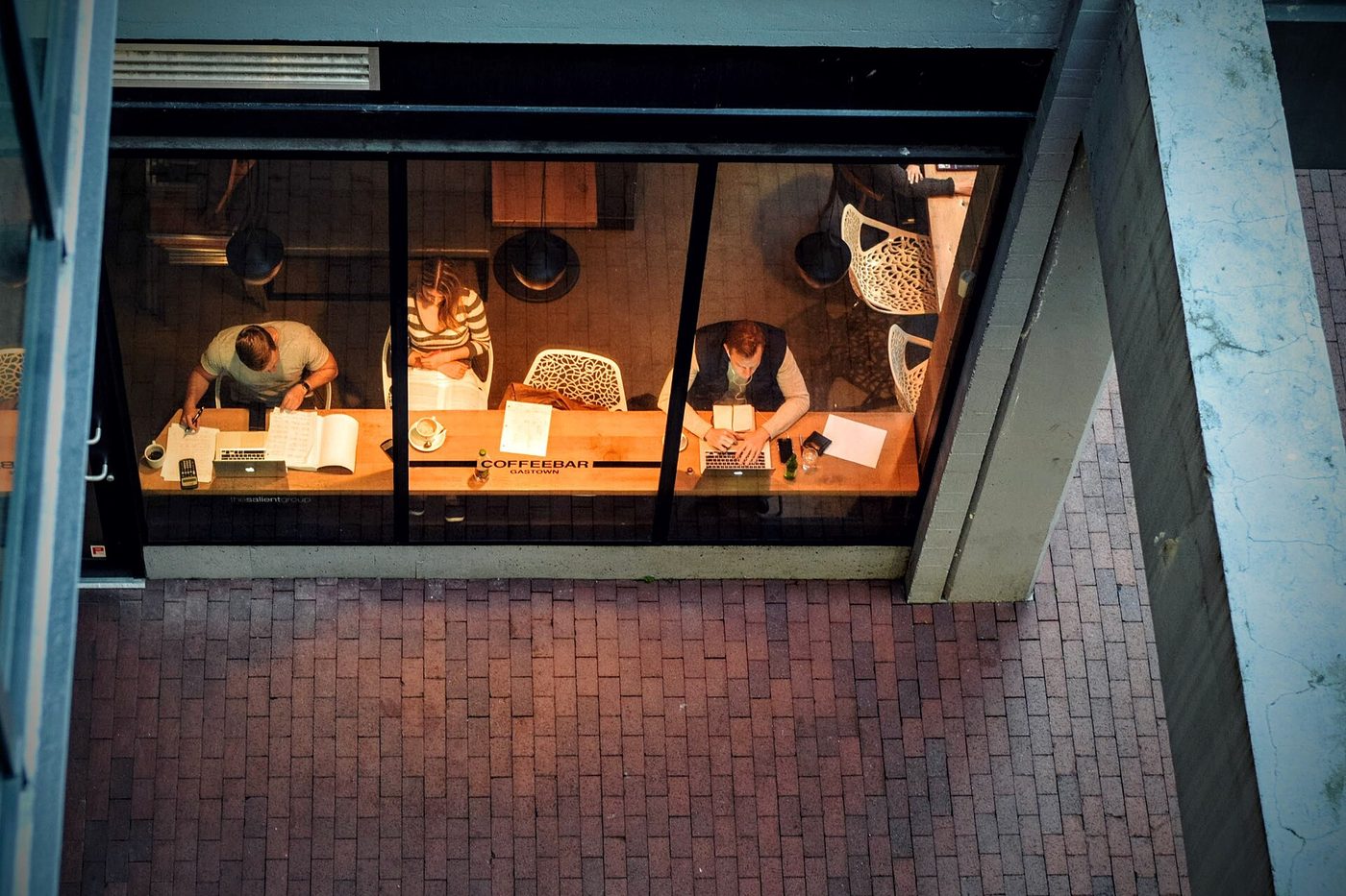 A busy coffee shop in Gastown, Vancouver, seen through a window from above, with people seated at tables.