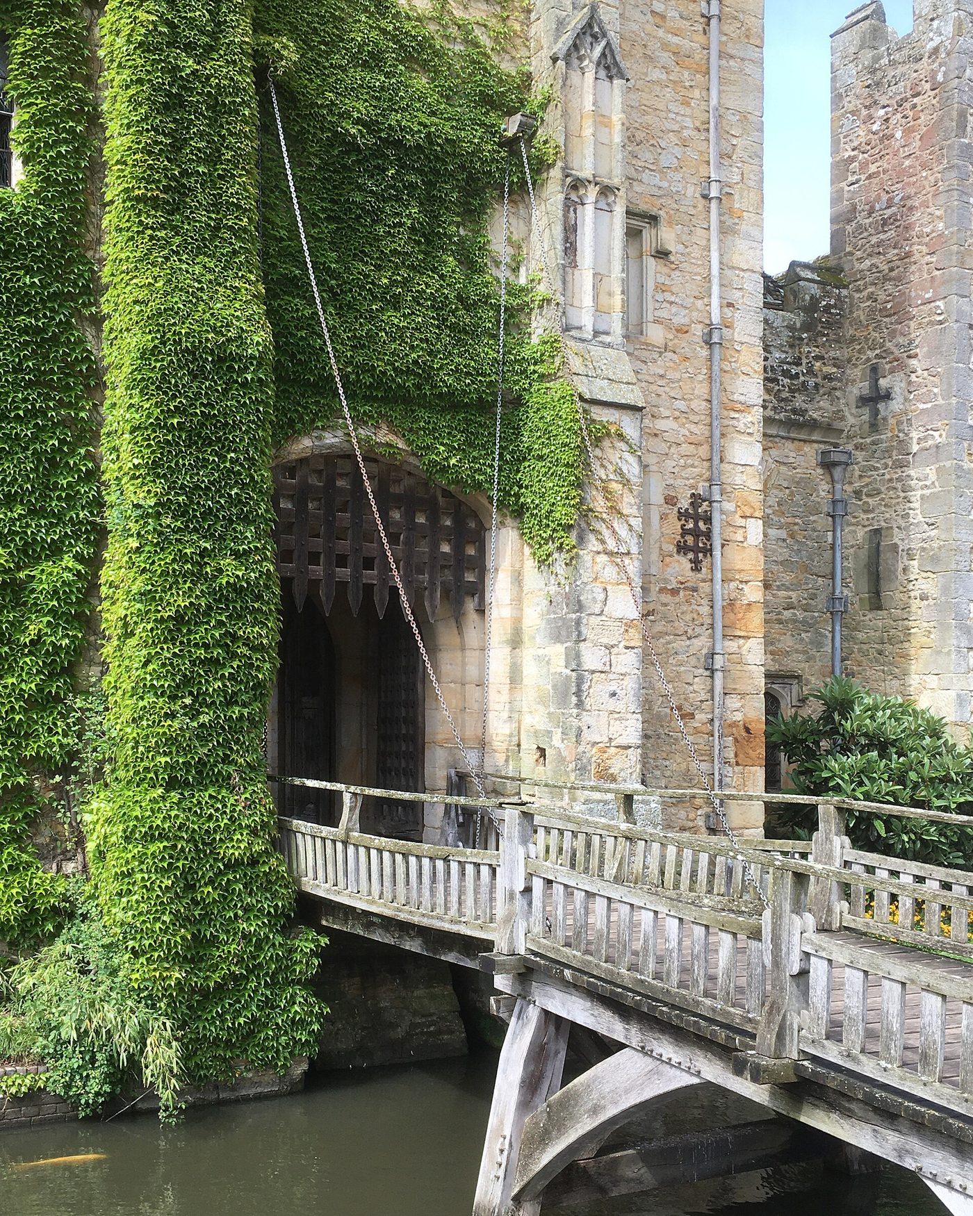 The stone gatehouse of Hever Castle in Kent with its raised portcullis, chains and wooden drawbridge over the moat.