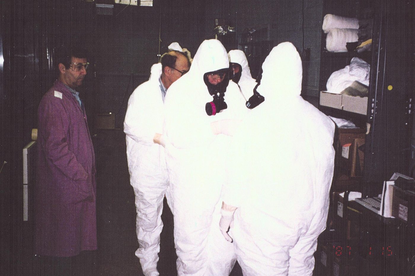 Workers in white full-body protective suits and respirators inside a containment structure at a U.S. Department of Energy facility.