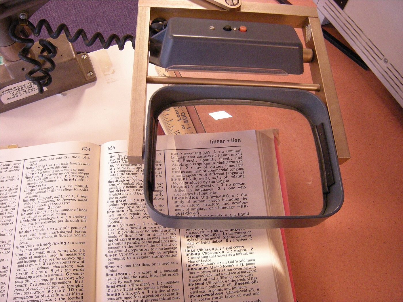 A rectangular magnifying glass held over a page of a dictionary at a library for blind and print-disabled readers.