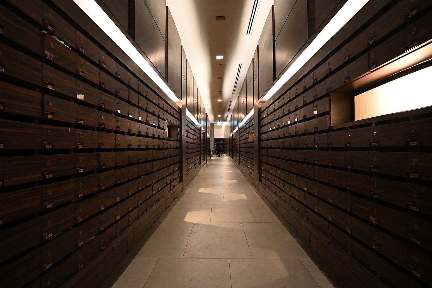 A long, dimly lit corridor lined floor to ceiling with rows of dark wooden mailboxes.