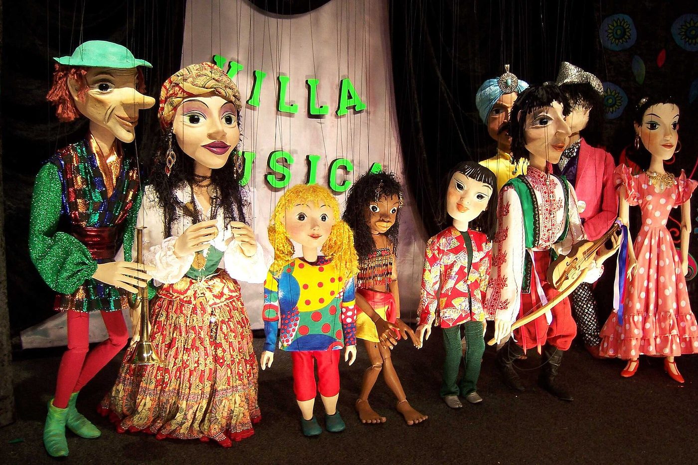A row of brightly costumed wooden marionettes hanging on display at a puppet theatre.