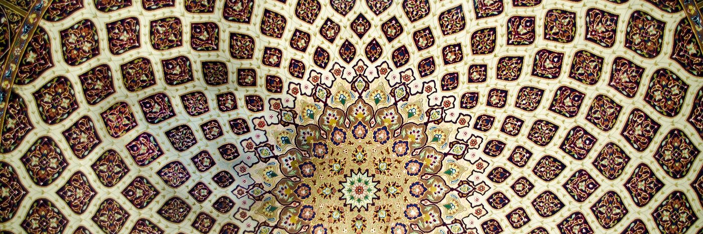 Top-down view of an ornate Persian carpet with a central medallion and repeating red and cream lattice pattern.