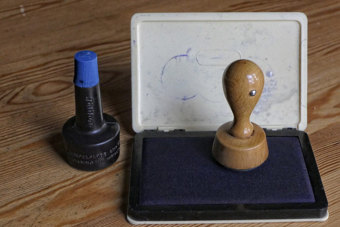 A wooden rubber stamp standing beside an open ink pad and a bottle of stamp ink on a wooden table.