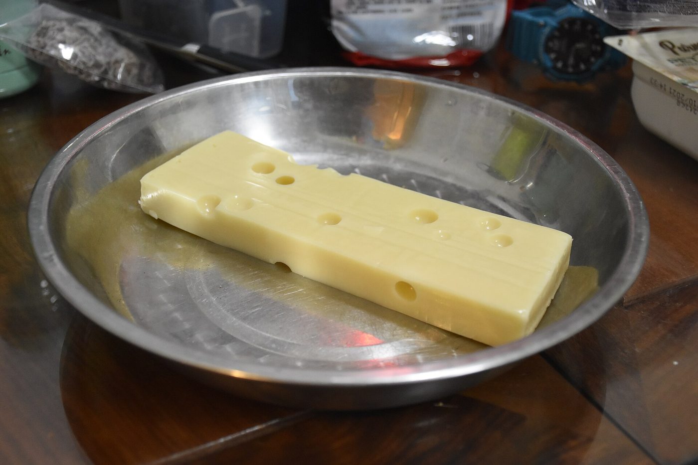 A block of Emmental cheese with round holes, sitting on a stainless steel plate.