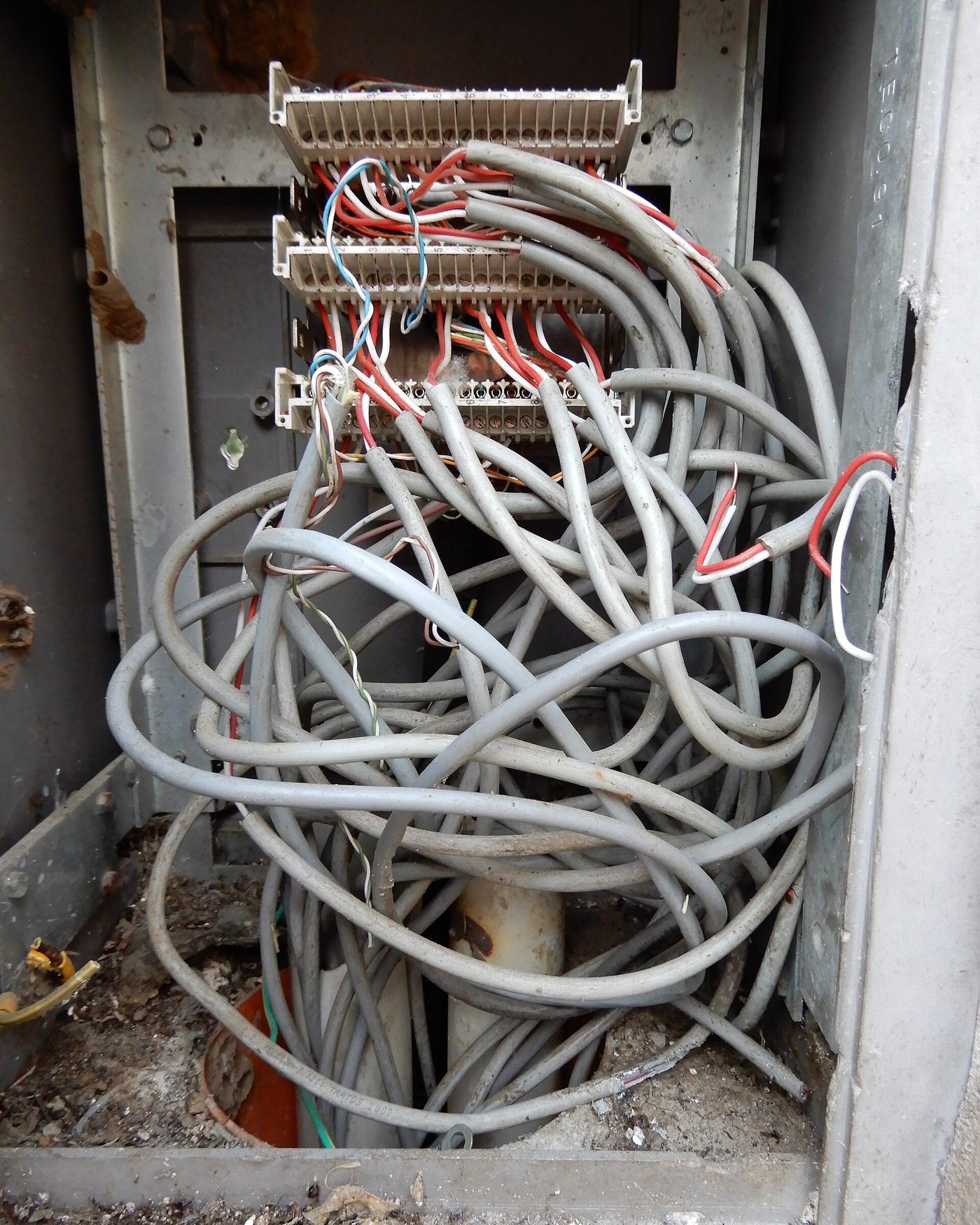 An open telecom cabinet with a tangle of grey and multicoloured wires spilling out of it.