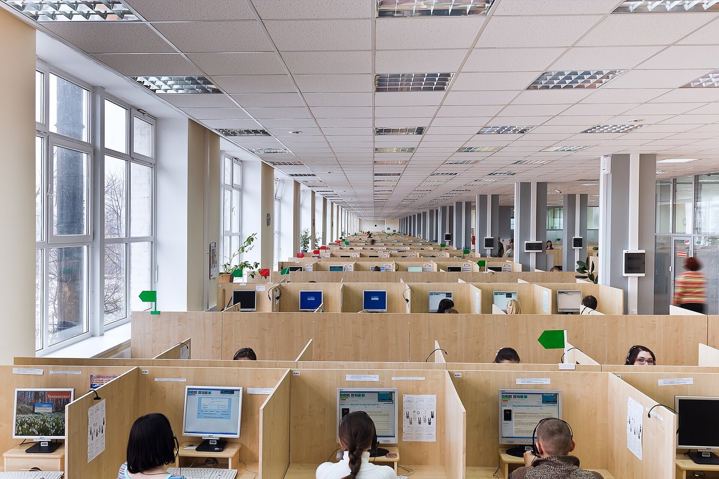 Un grand centre d’appels lumineux à aire ouverte à Orel, en Russie, où des agents munis de casques travaillent à des rangées de bureaux cloisonnés.