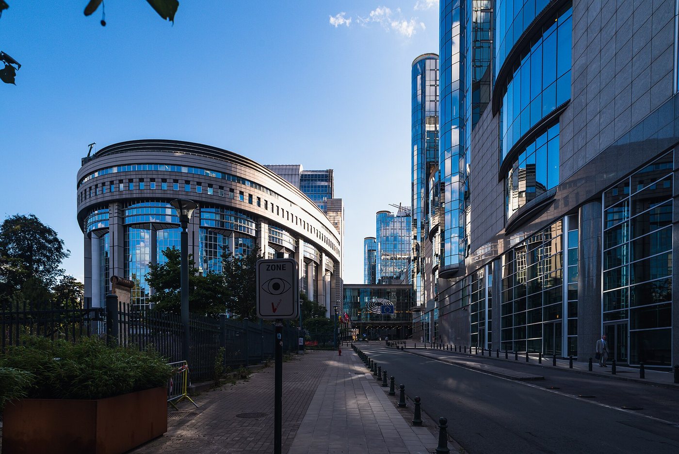Le bâtiment Paul-Henri Spaak du Parlement européen à Bruxelles, tout en verre incurvé, à côté de tours de bureaux modernes sous un ciel bleu.