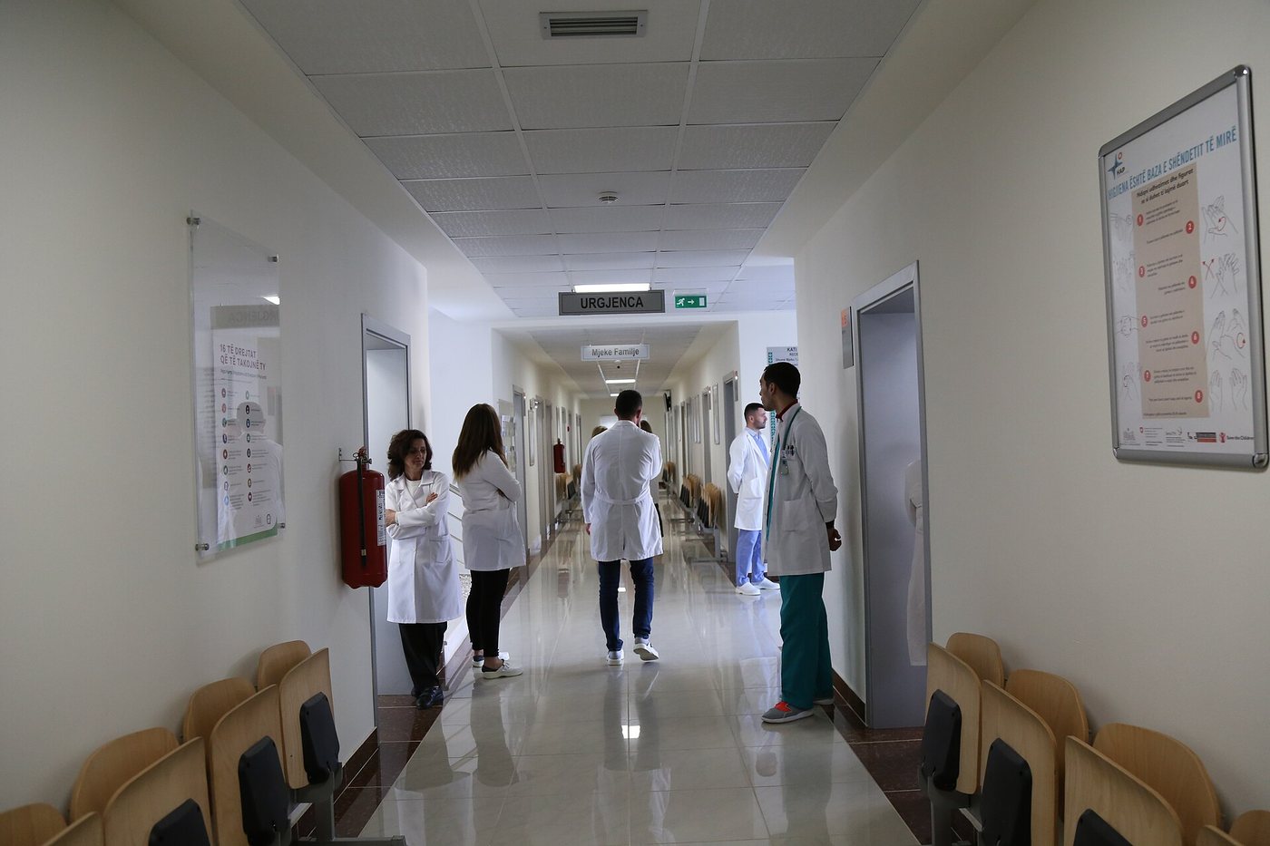 Un corridor lumineux dans un centre de santé rénové à Patos, en Albanie, avec du personnel médical en blouse blanche qui s’éloigne et des chaises d’attente le long des murs.