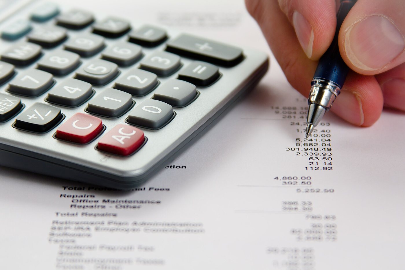 Gros plan d’une main qui vérifie avec un stylo les chiffres d’un relevé financier imprimé, à côté d’une calculatrice de bureau.