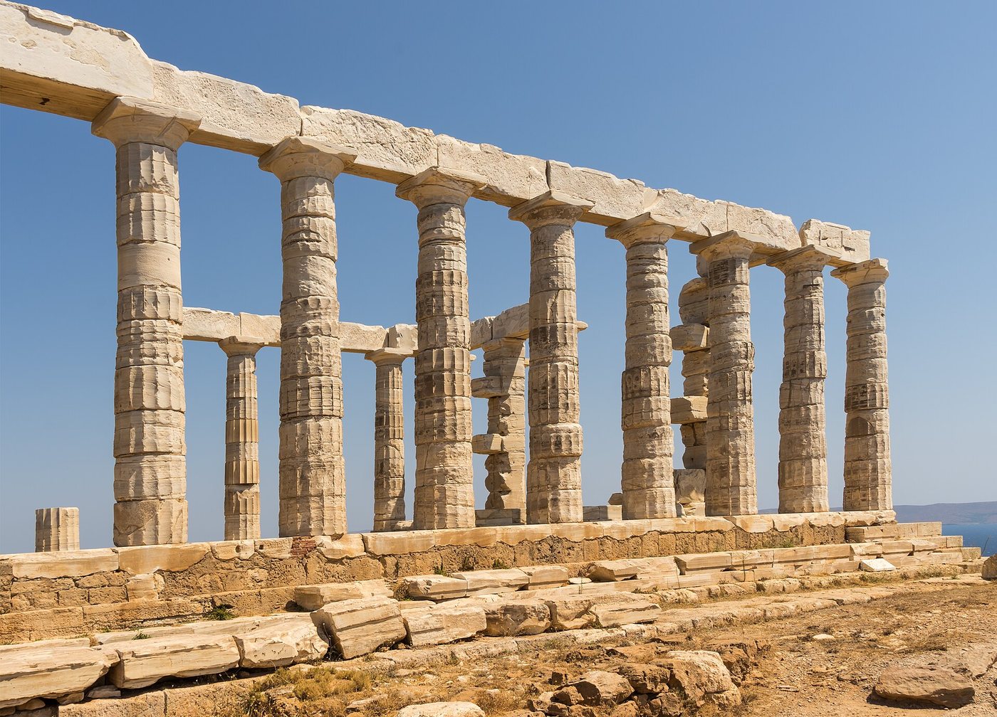 Colonnes doriques en marbre patiné du temple de Poséidon au cap Sounion, en Grèce, vues en perspective sur un ciel bleu.