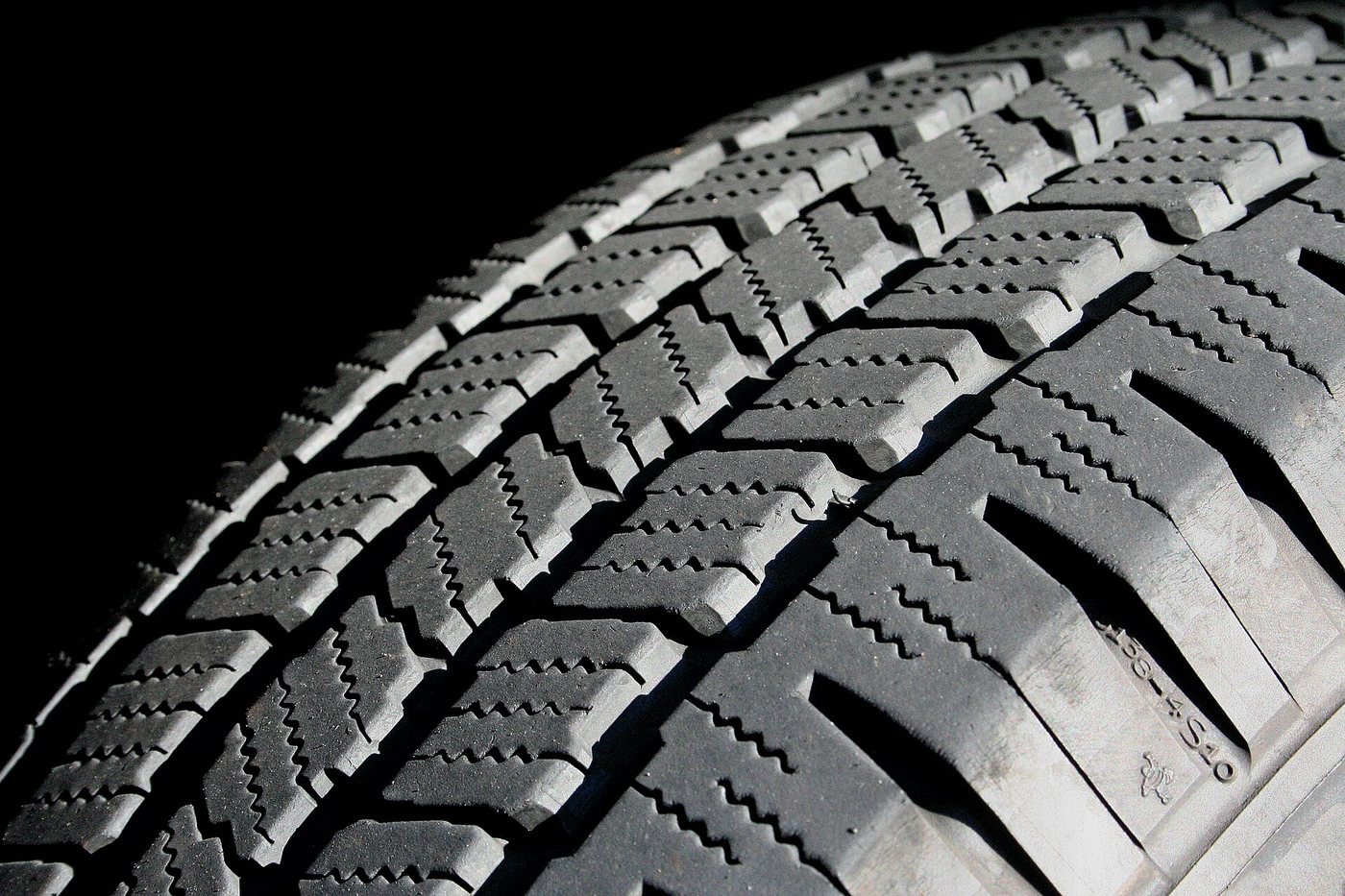 Gros plan des pains de la bande de roulement d’un pneu de voiture, sur fond noir.